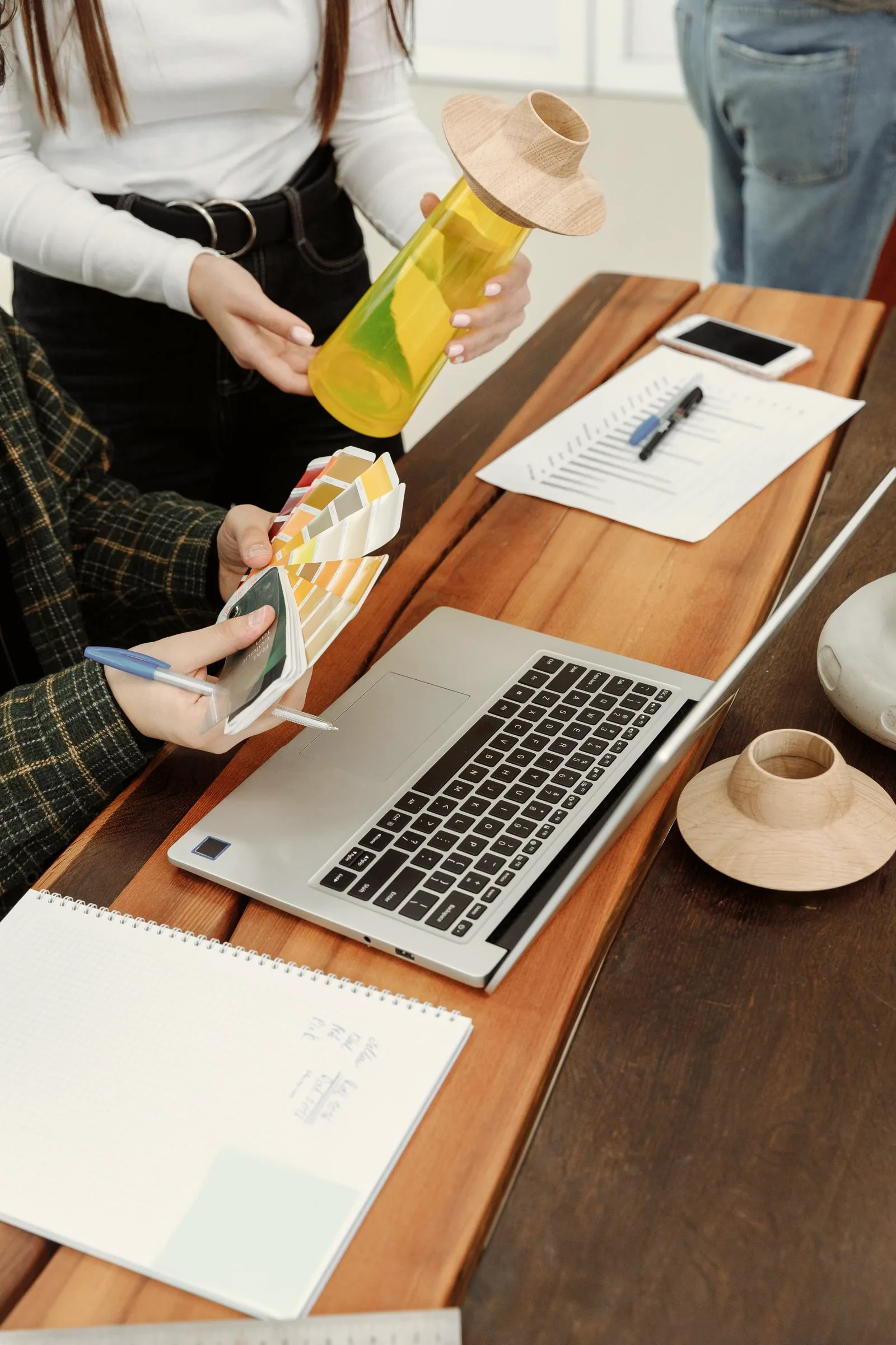 Hands holding colour swatches over a desk with a laptop