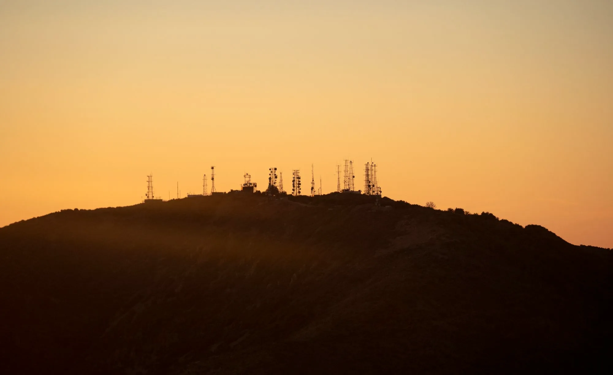 Telecom towers silhouetted on a hilltop at sunset