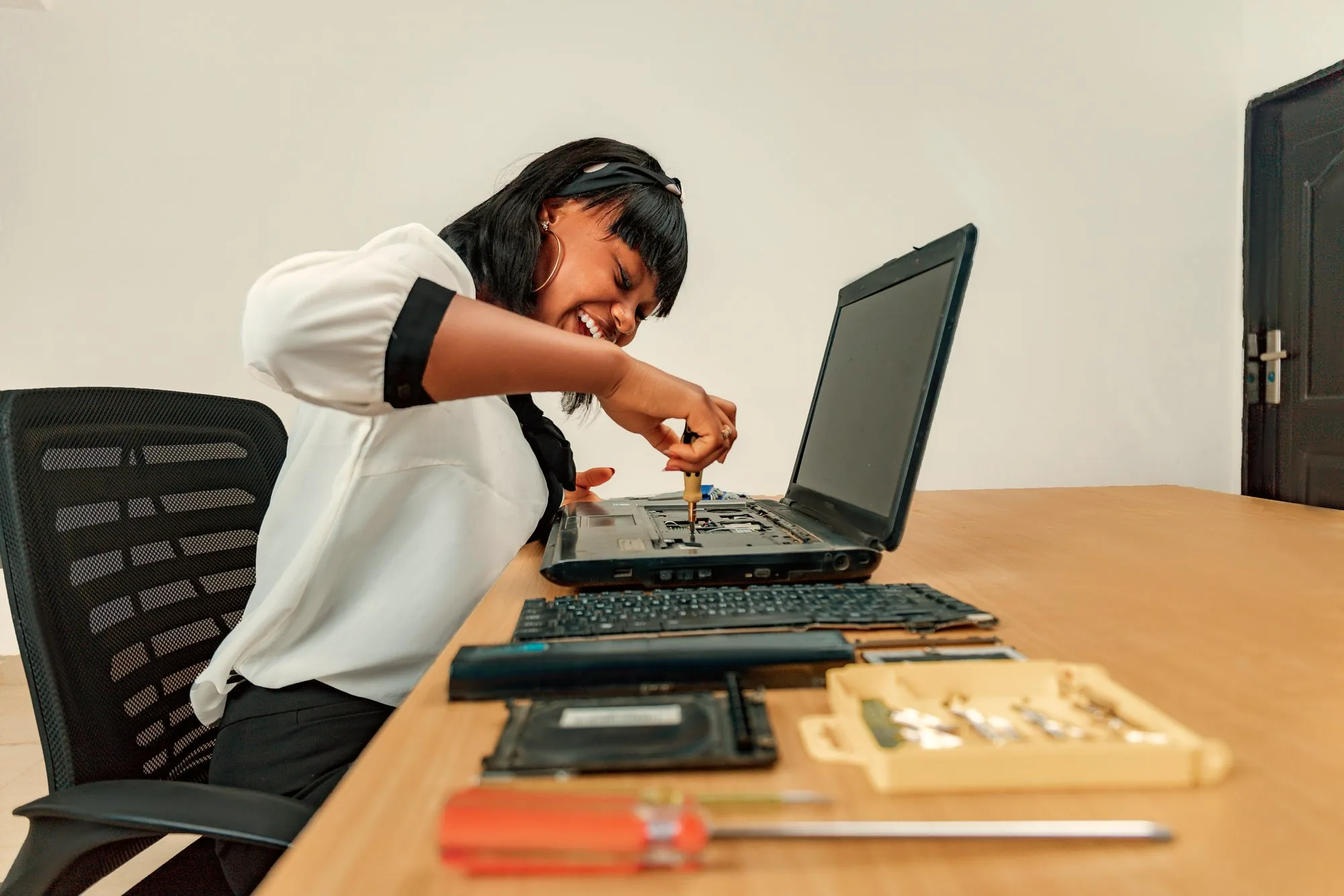 Woman repairing an opened laptop with tools on a desk